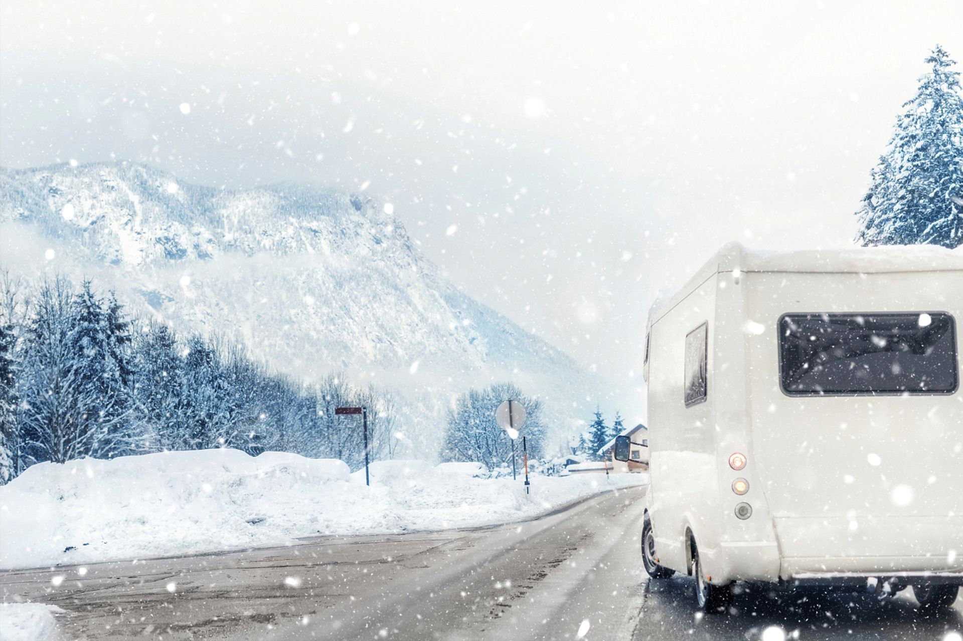 Rear view of an RV driving through snow with snow-covered mountains and trees in the background